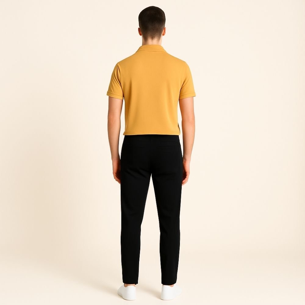 Person wearing a mustard yellow polo shirt and black pants on a beige background