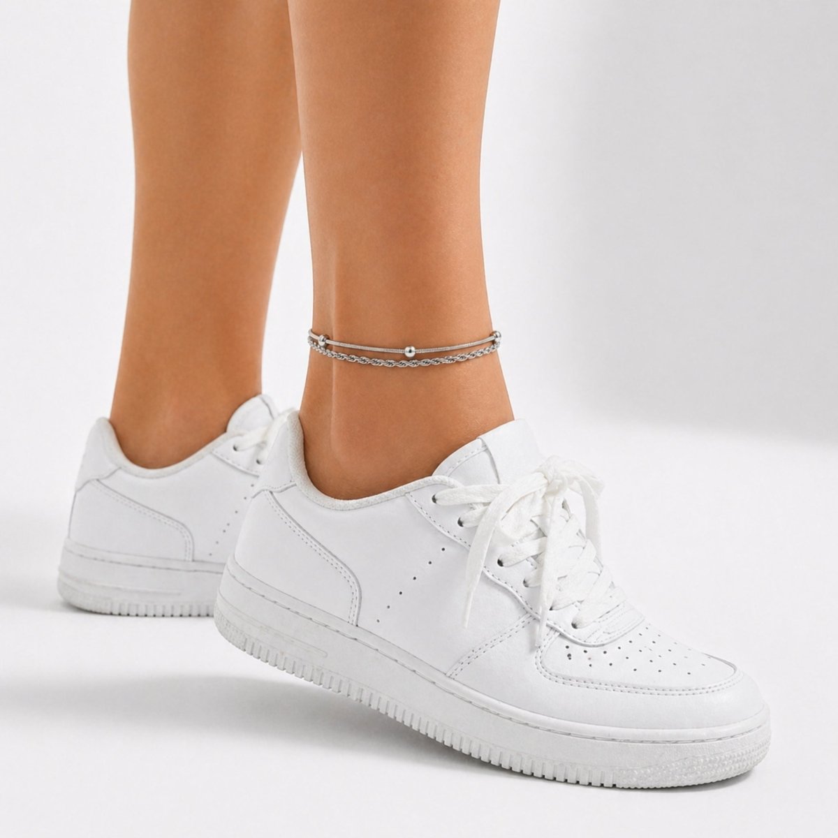 Side profile of a woman walking in white sneakers to showcase the Kouvr layered silver anklet.