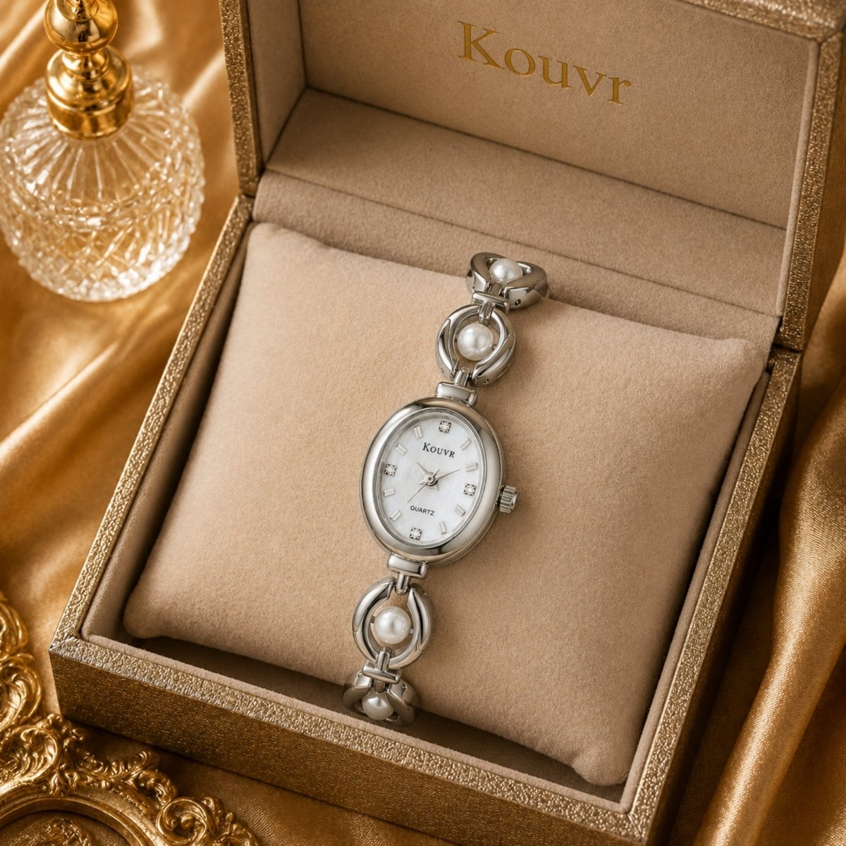Kouvr silver tone pearl watch resting inside an elegant beige presentation box next to a crystal perfume bottle.