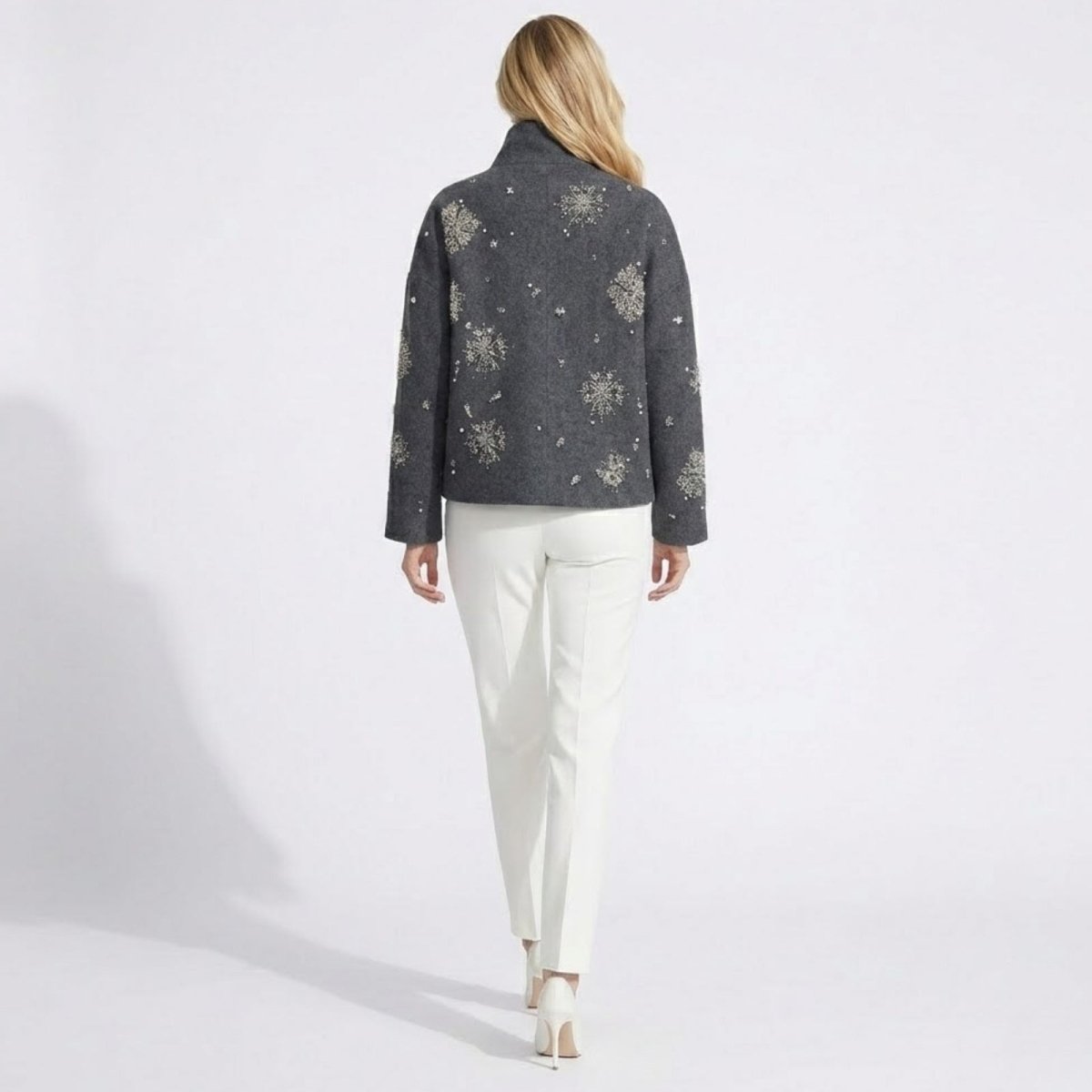 Back view of a female model wearing the Kouvr dark grey jacket, showcasing the intricate snowflake beadwork across the back and sleeves.