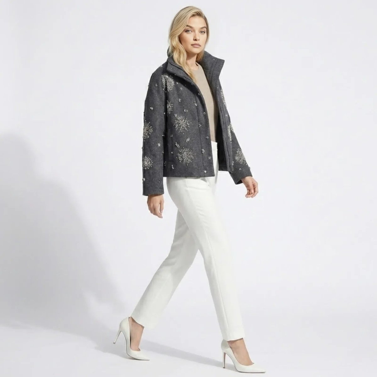 Side profile of a female model walking while wearing the Kouvr dark grey embellished snowflake jacket, showing sleeve detail and garment movement.