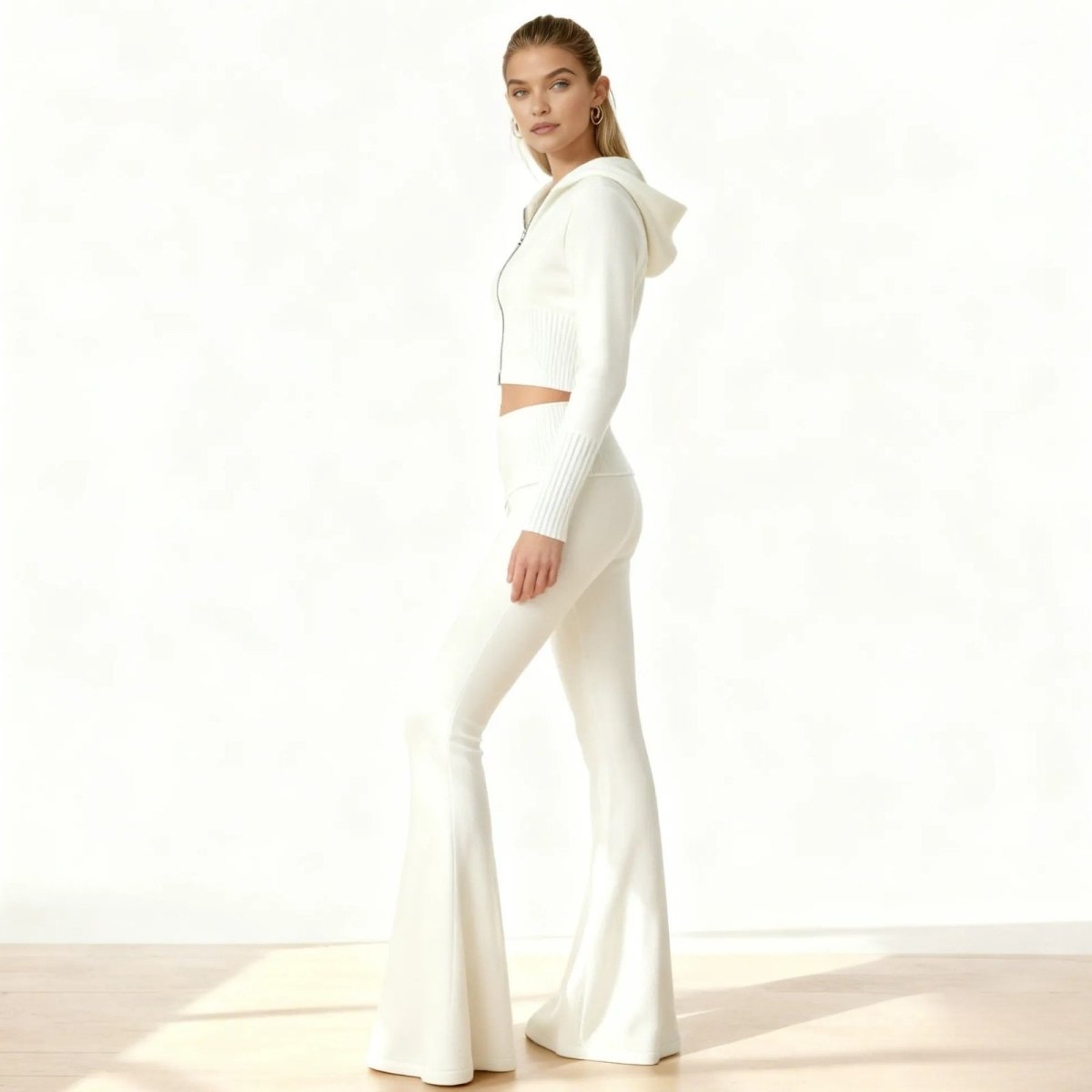 Side profile of a model in a white luxury knit loungewear set showing the fit of the cropped zip hoodie and flared pants.