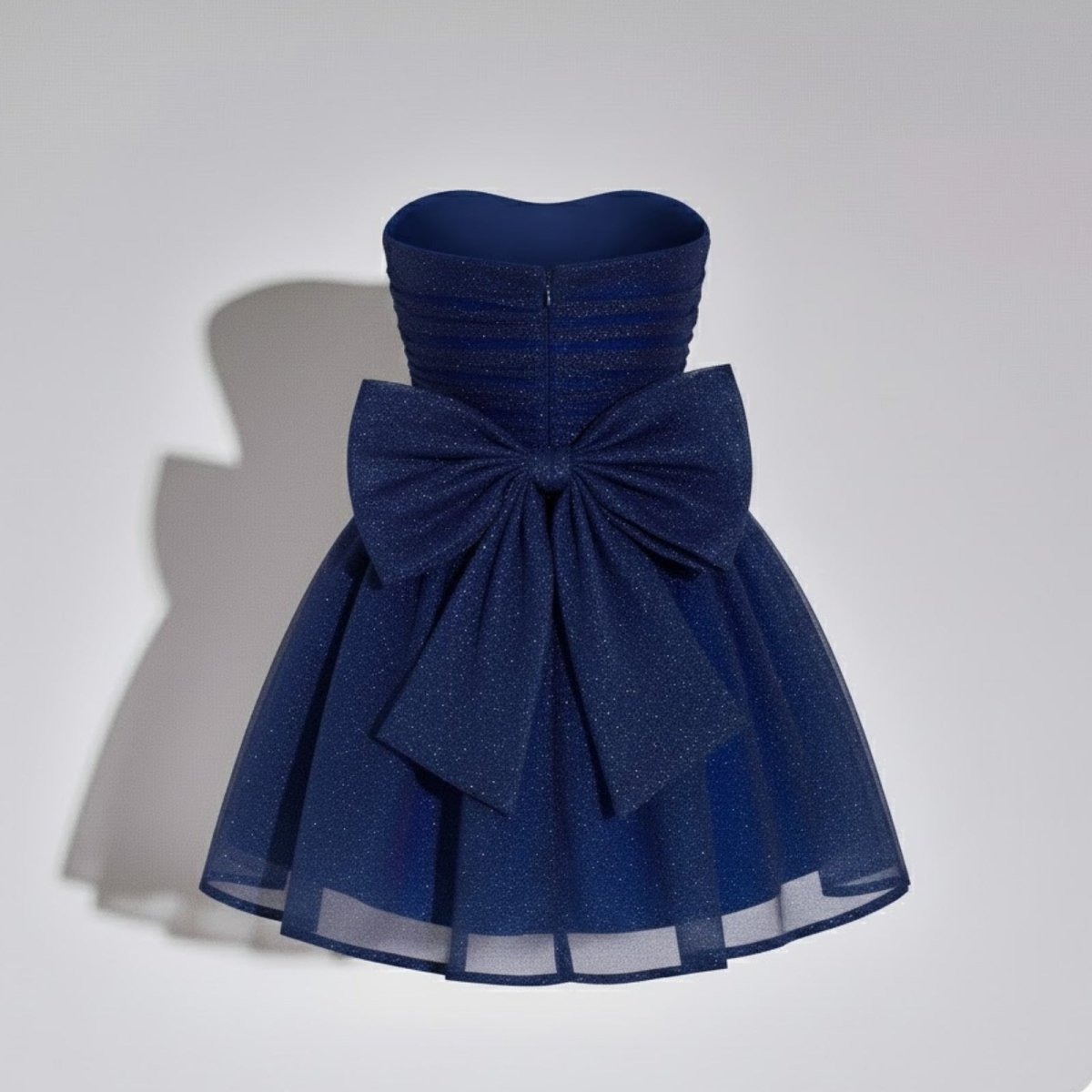 Product shot of the back of a dark blue strapless glitter dress, highlighting the oversized bow and zip closure.