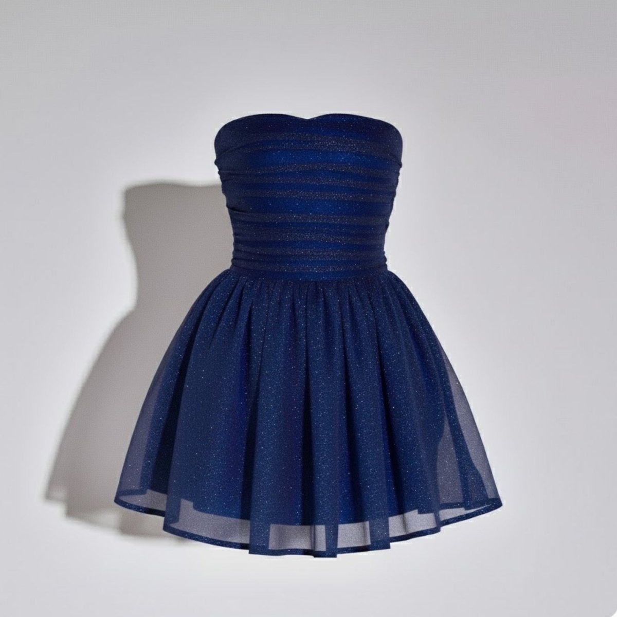 Product shot of a dark blue strapless cocktail dress with a glitter finish and ruched bodice on a white background.
