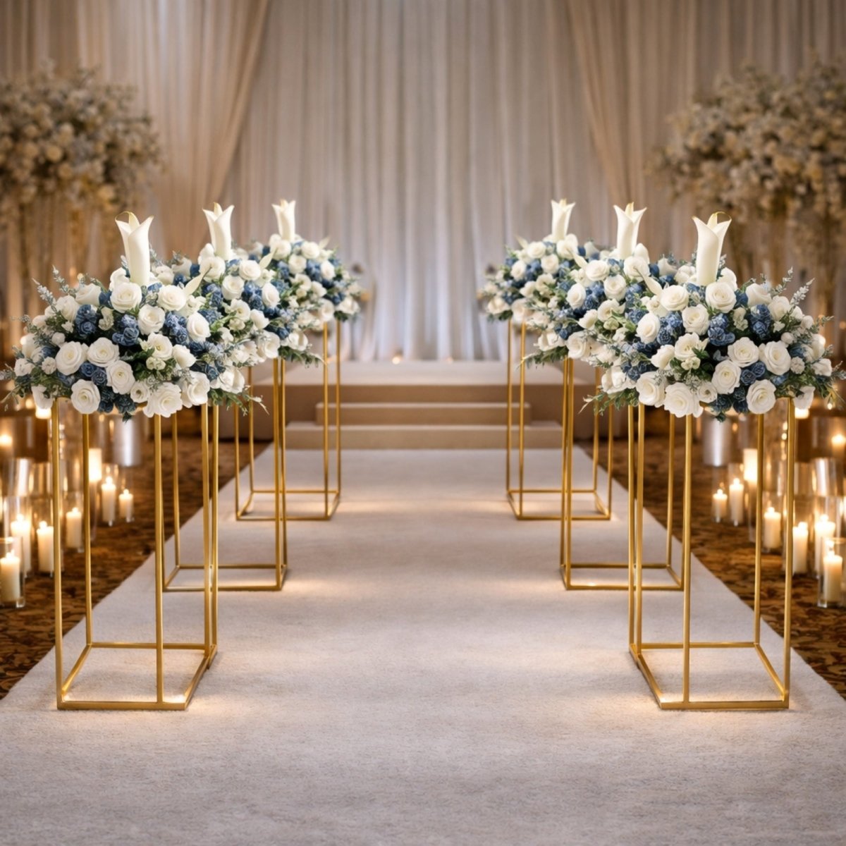 An elegant indoor wedding ceremony aisle with a white runner, flanked by tall gold geometric stands holding white and blue floral arrangements and surrounded by candles.