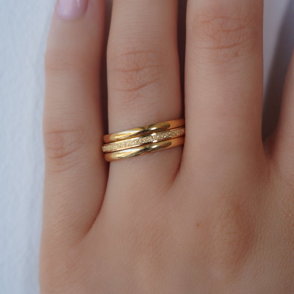 Kouvr Tavia Gold Stacking Ring Set on a woman's hand.", "Close up detail of the Kouvr Stardust textured gold ring.", "Lifestyle image of the three-piece Kouvr gold ring set.