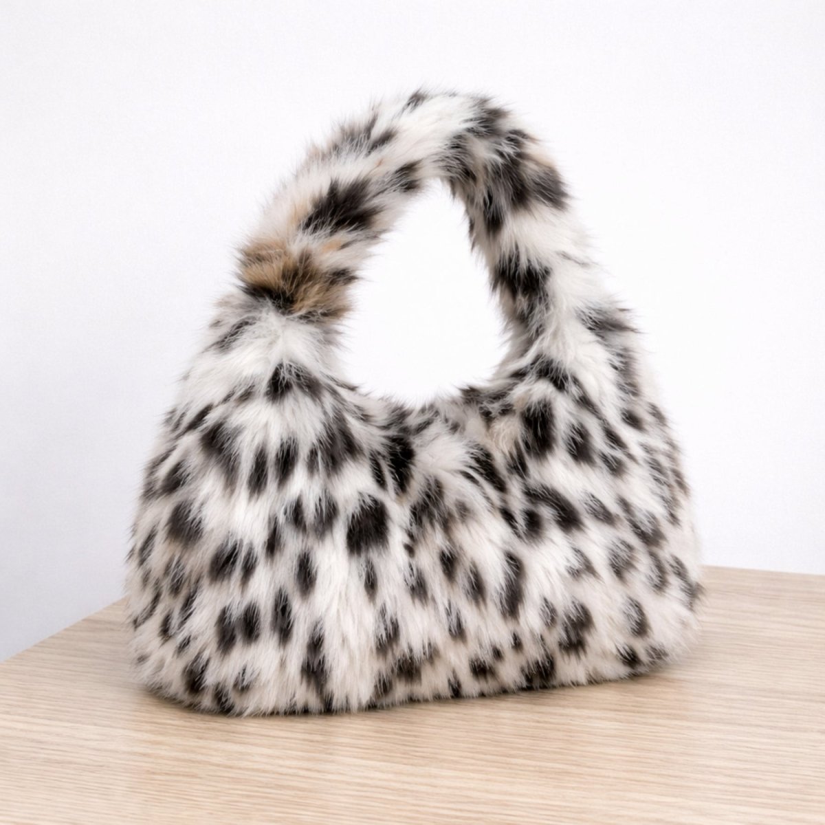 Side profile of the Kouvr Thaila fuzzy snow leopard print handbag sitting on a light wood table.