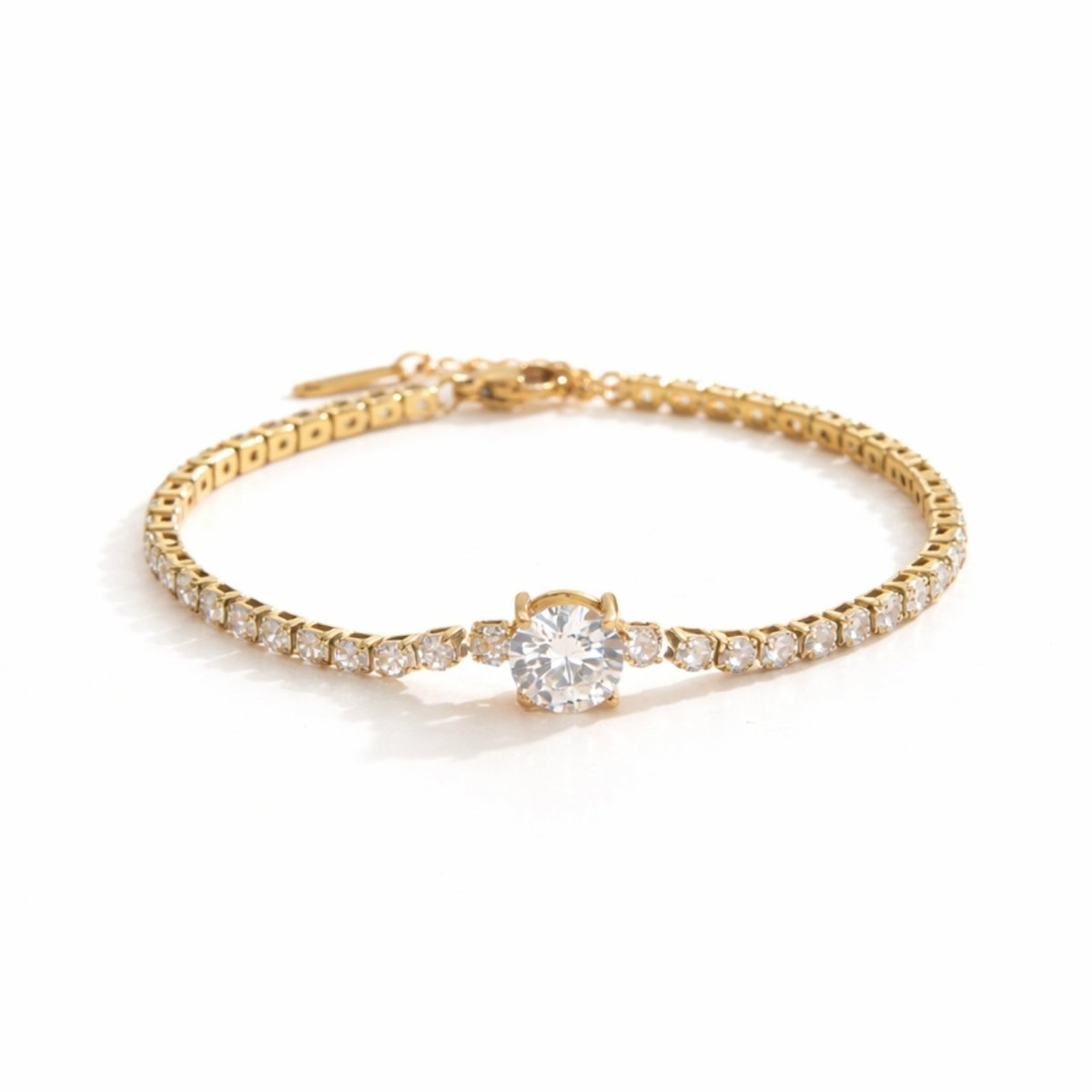 Thalira gold solitaire tennis bracelet with a large central round cut crystal on a white background by Kouvr.