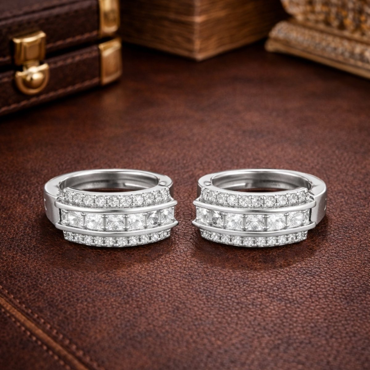 Frontal view of the pair of Kouvr silver diamond huggie earrings sitting side-by-side on a textured brown leather surface.