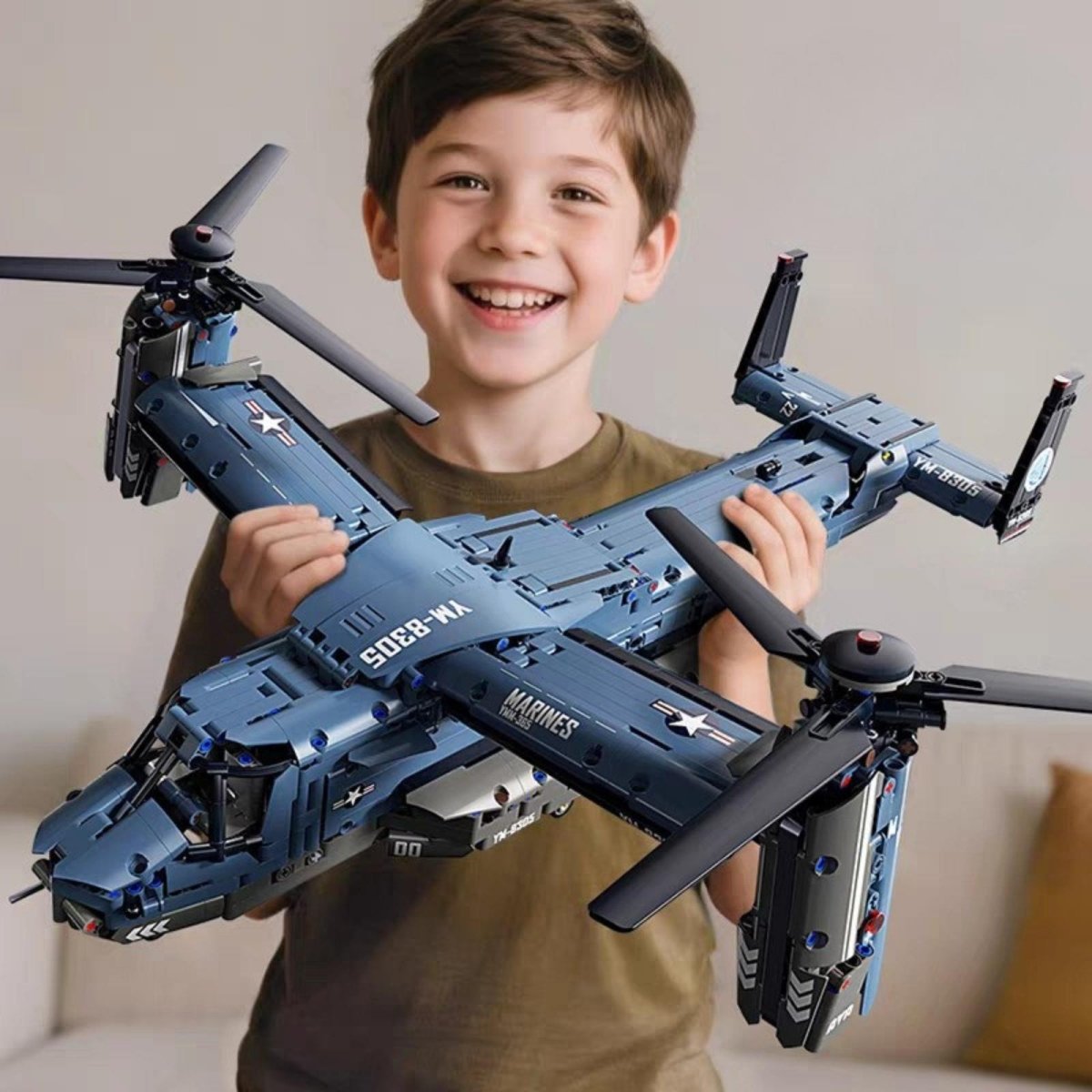 A smiling boy proudly holding up his completed V-22 Osprey building block toy, showing its large scale and intricate details.