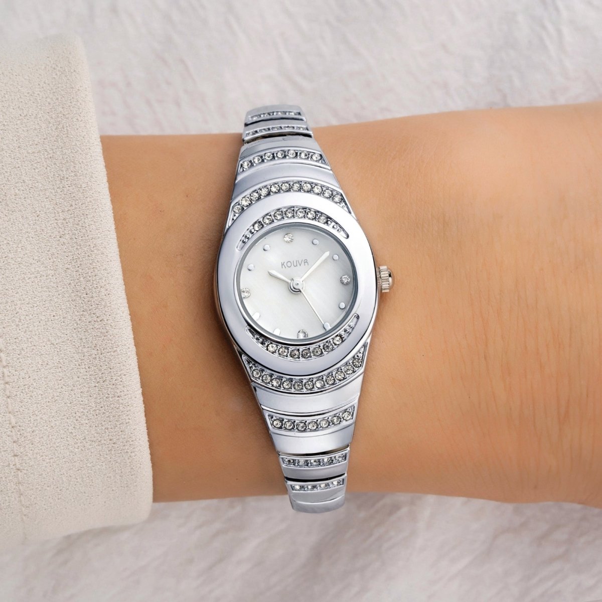 Silver kouvr wristwatch with gemstone accents on a wrist against a neutral background