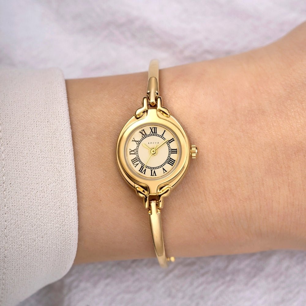 Gold Kouvr wristwatch with a white face and black Roman numerals on a wrist.
