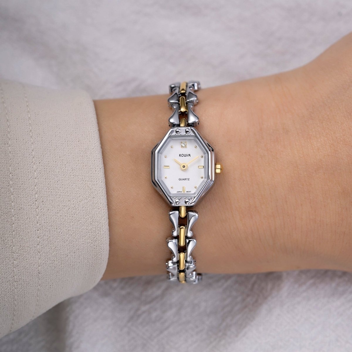 Silver and gold kouvr watch on a wrist with a neutral background