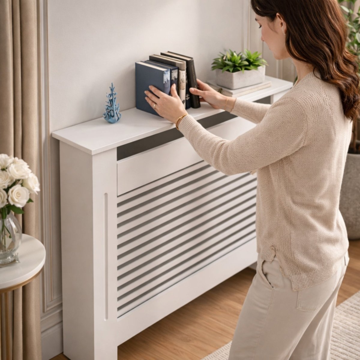 A woman in a neutral sweater arranges books on a modern white slatted radiator cover being used as an elegant console shelf in a warmly lit living room.