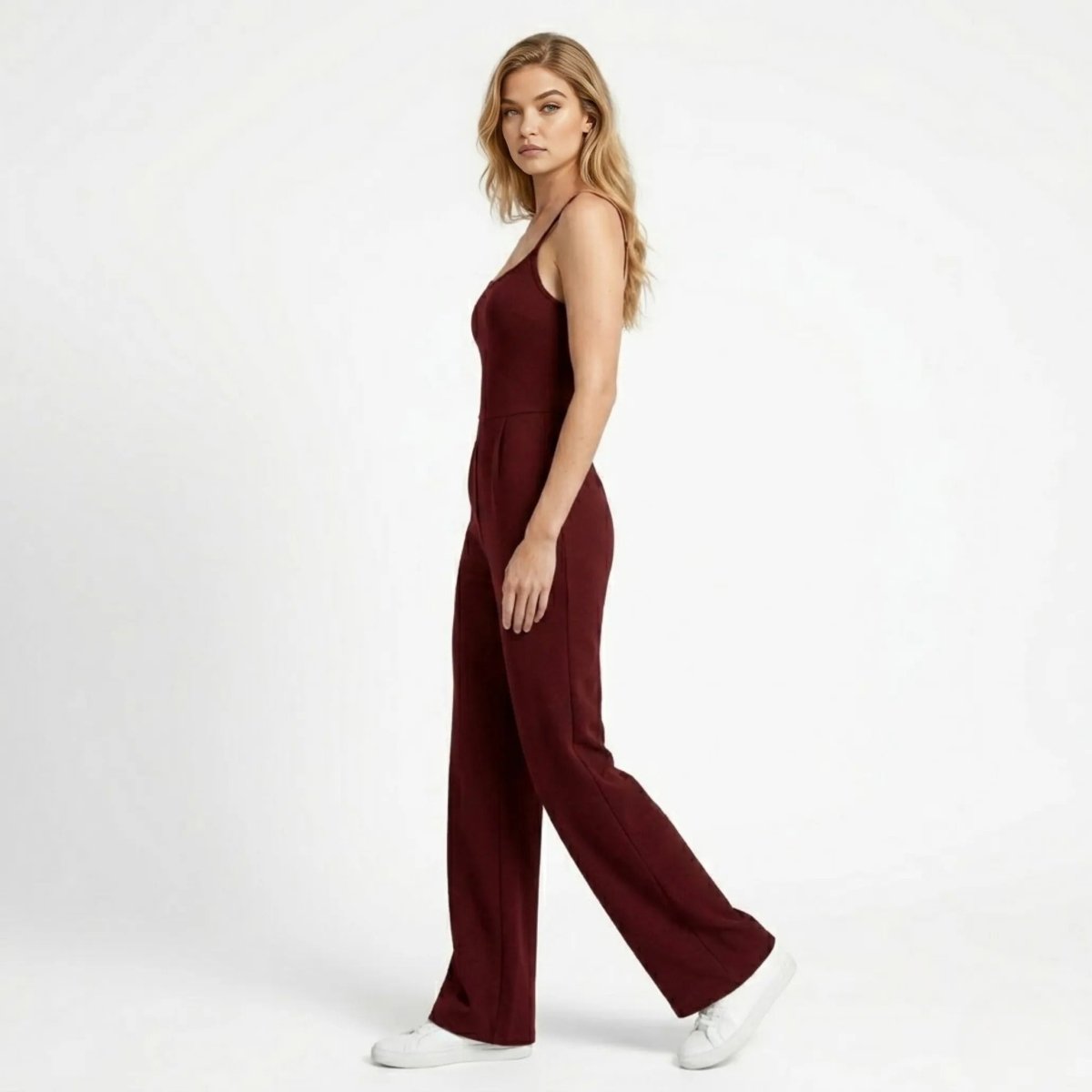 Side profile of woman walking in Kouvr wine red wide leg strappy jumpsuit showing fluid drape and fit.