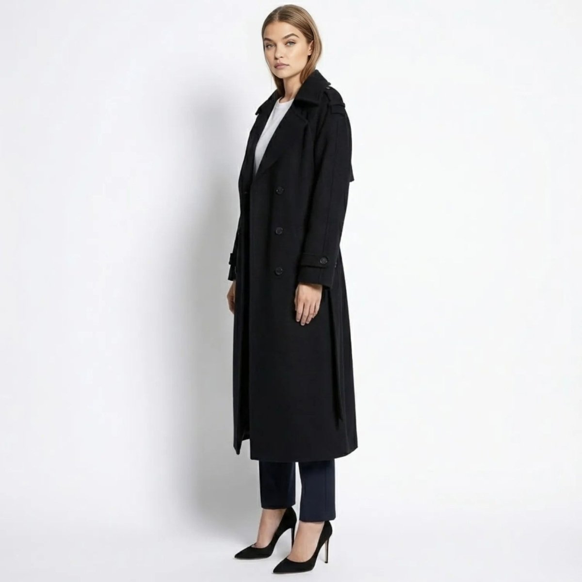 Side profile of the Kouvr women's black wool trench coat, highlighting its long silhouette, epaulettes, and belted cuff details.