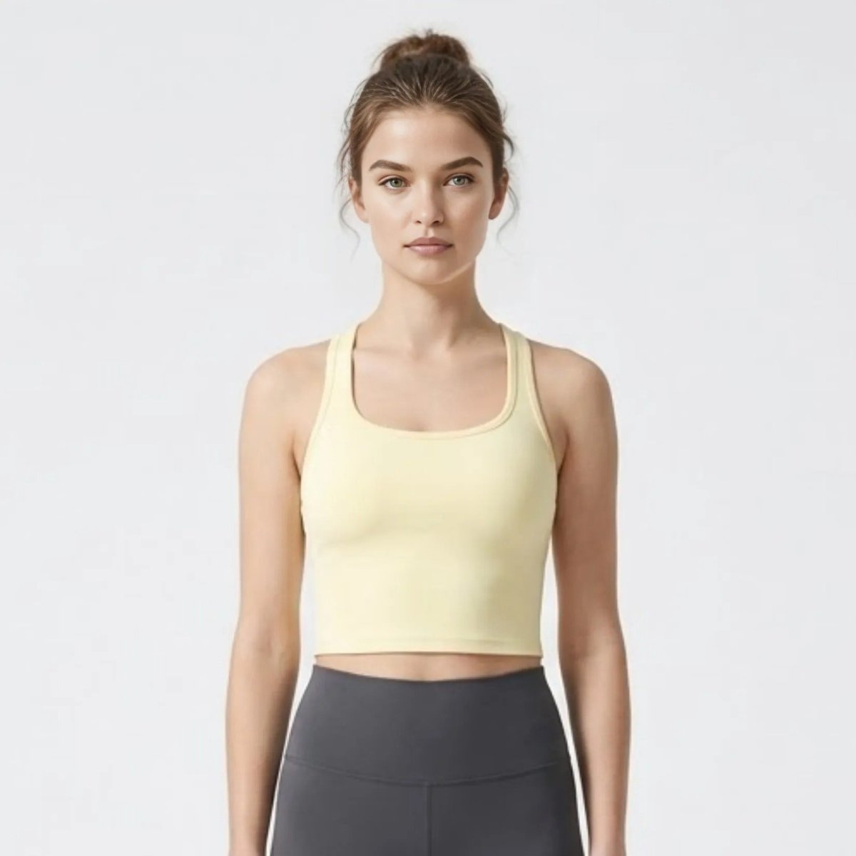 Woman wearing Kouvr pale yellow racerback cropped tank top paired with dark grey high-waisted leggings facing forward