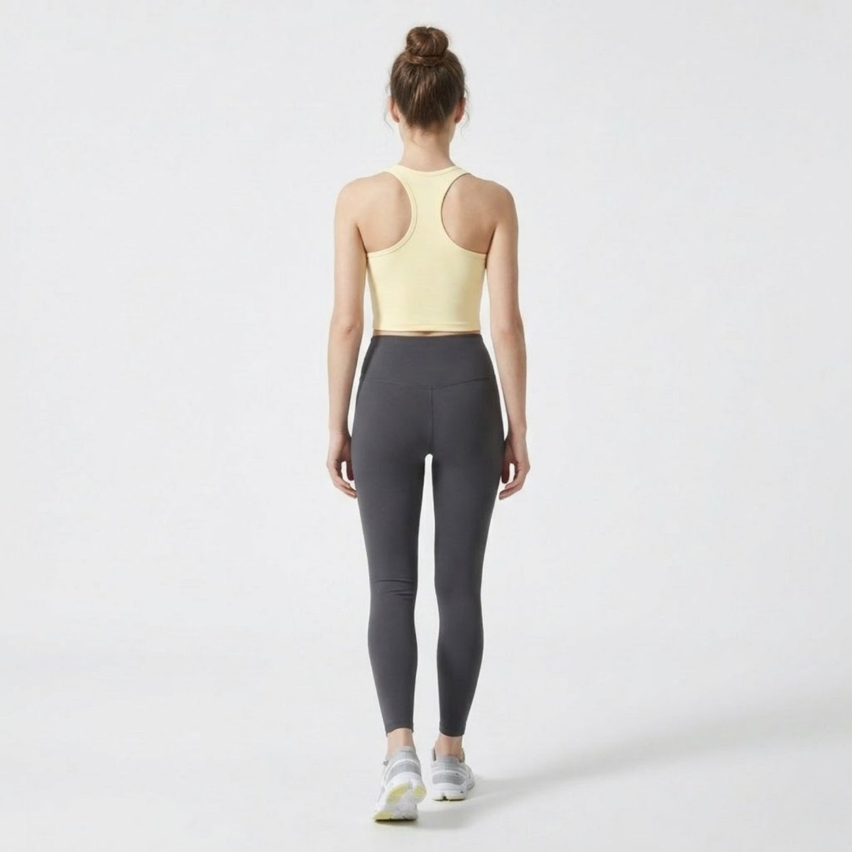 Full body back view of athletic woman wearing Kouvr yellow racerback gym top