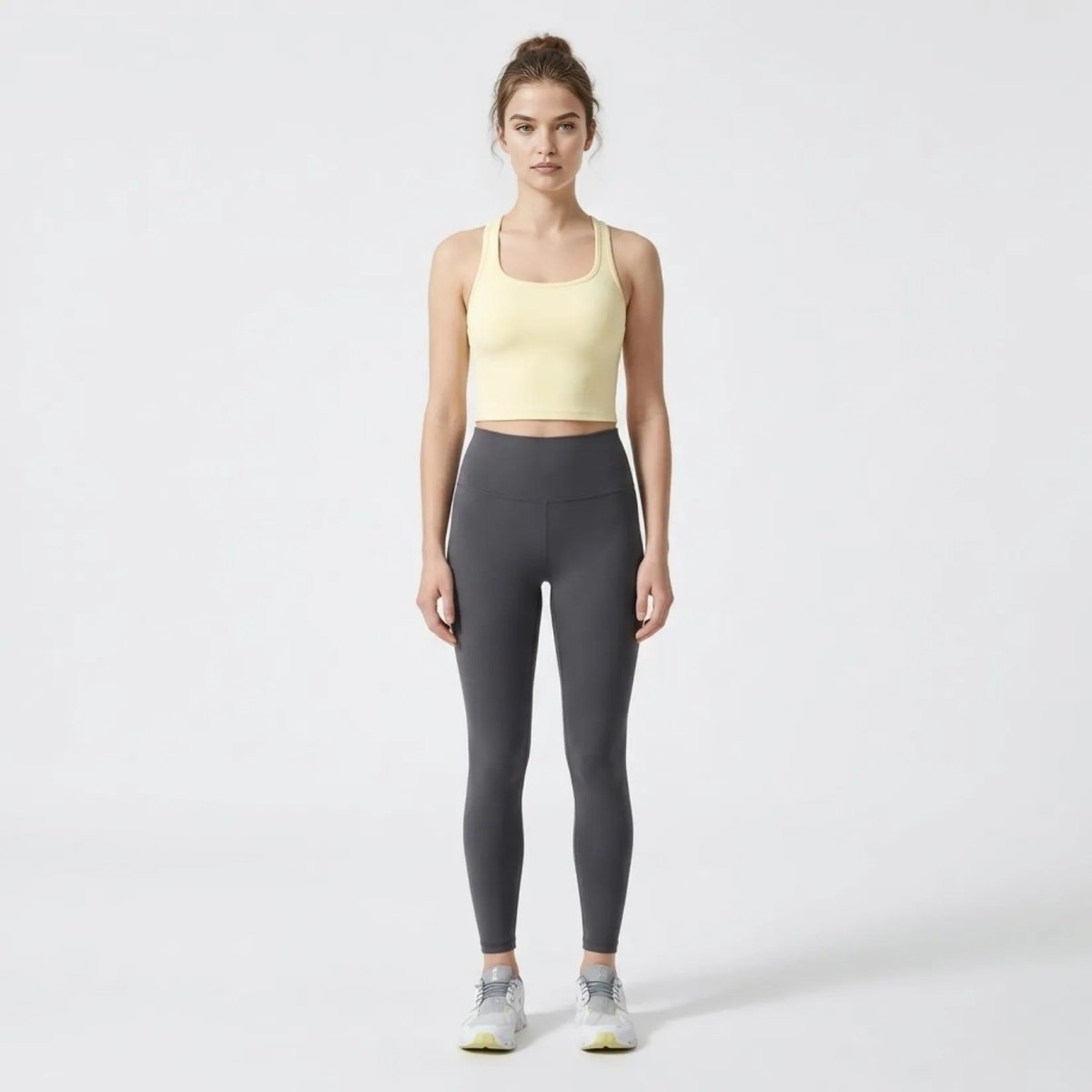 Full body studio shot of model wearing Kouvr luxury yellow athletic crop top and charcoal leggings