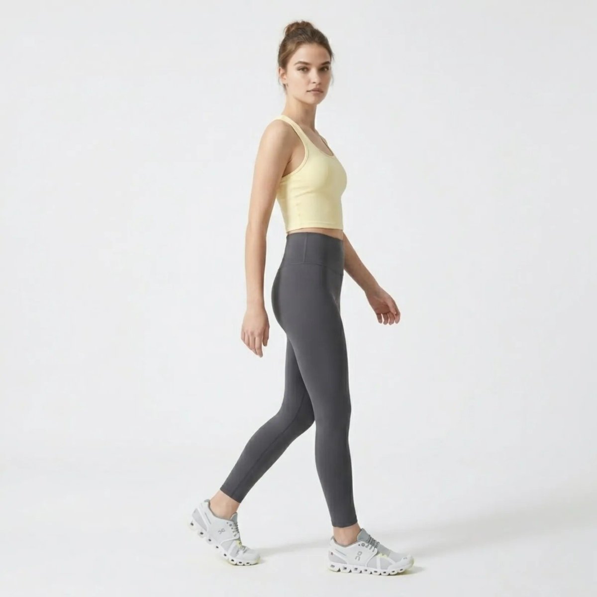 Side profile of woman walking in Kouvr fitted yellow cropped sports tank top and workout leggings