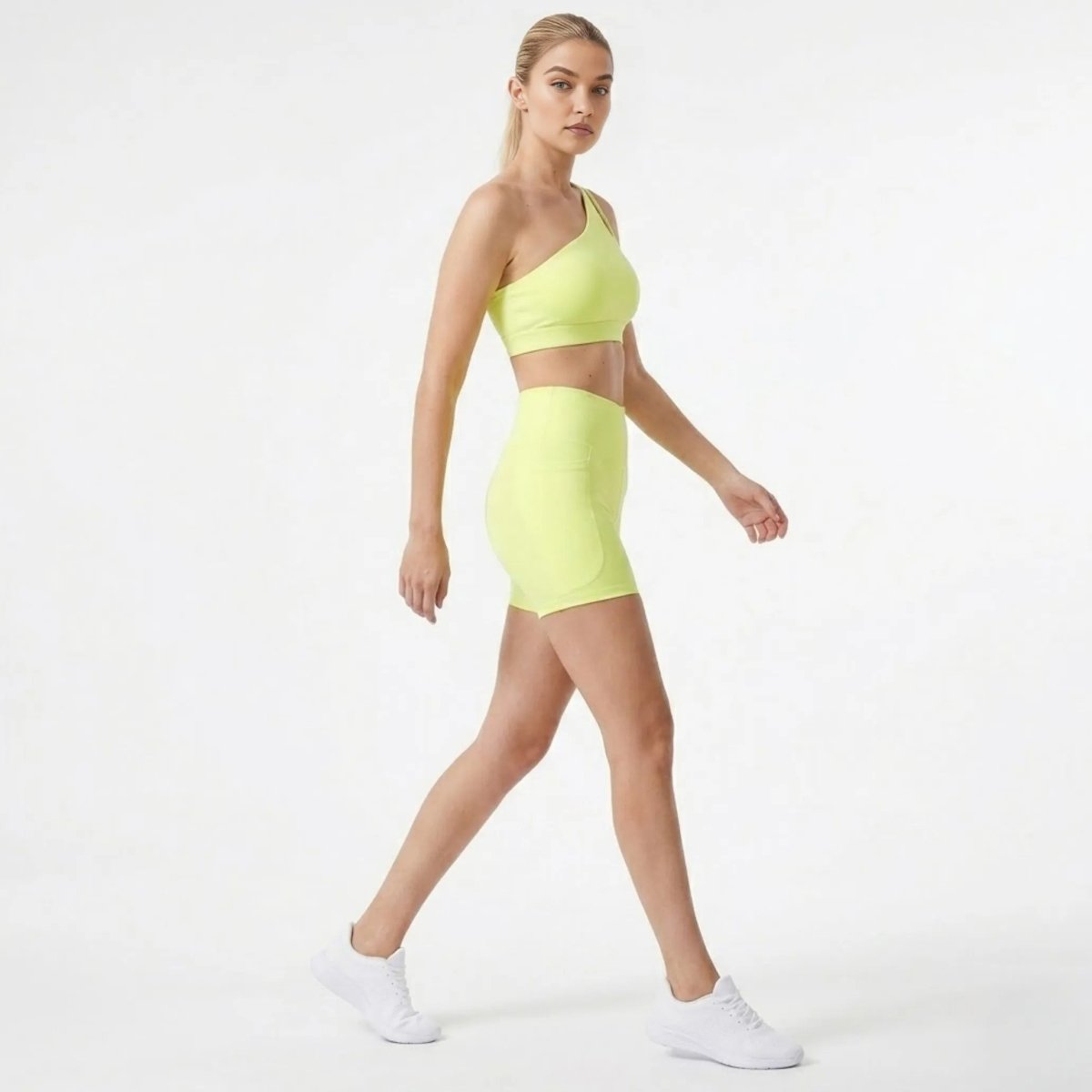 Side profile of model walking in Kouvr premium yellow matching workout set featuring high rise pocket shorts and one shoulder crop top