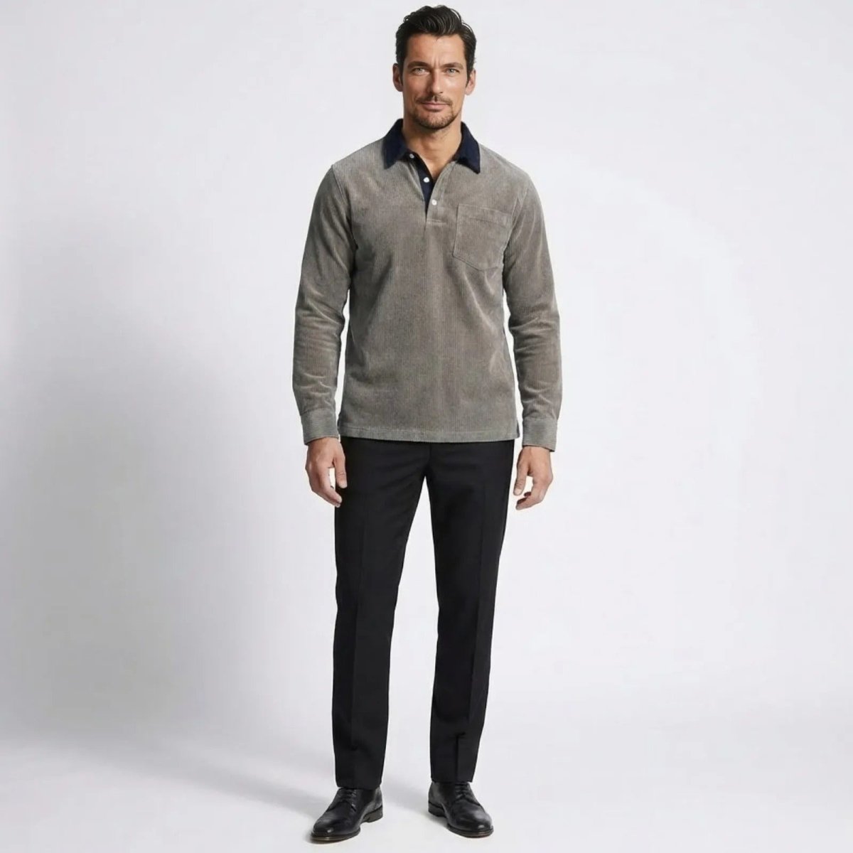 Model wearing the Kouvr Zain grey corduroy long sleeve polo shirt with a navy contrast collar, paired with black trousers, viewed from the front.