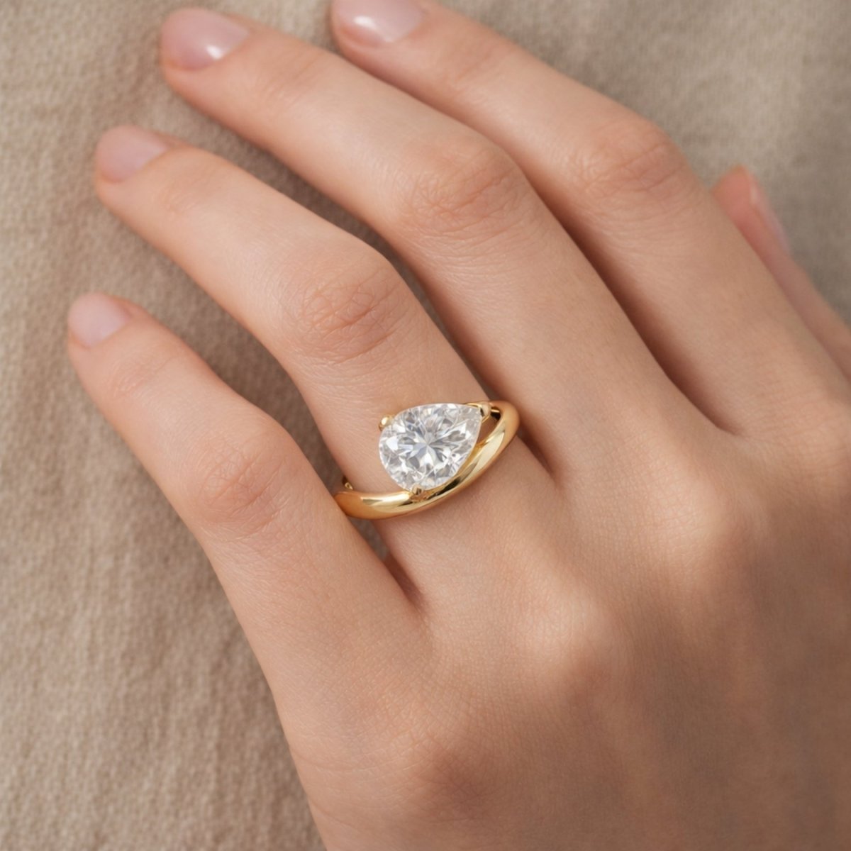 Angled detail shot of the Kouvr Zella pear cut solitaire ring on a finger, highlighting the brilliance of the stone and the polished gold band.