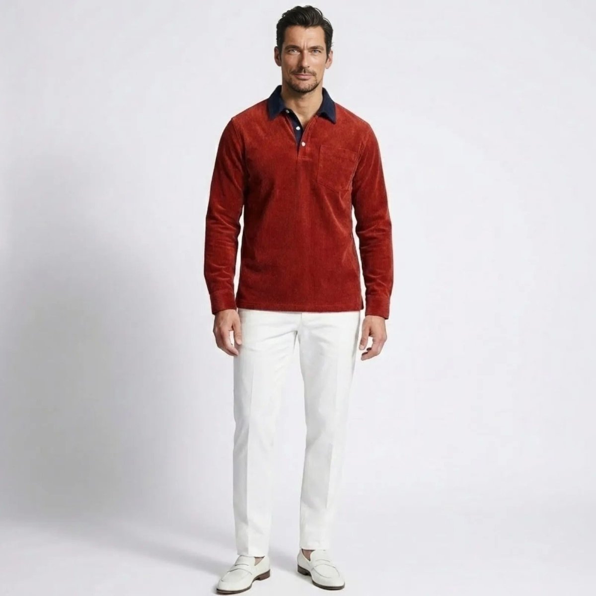 Model wearing the Kouvr Zian red corduroy long sleeve polo shirt with a navy contrast collar, paired with white trousers.