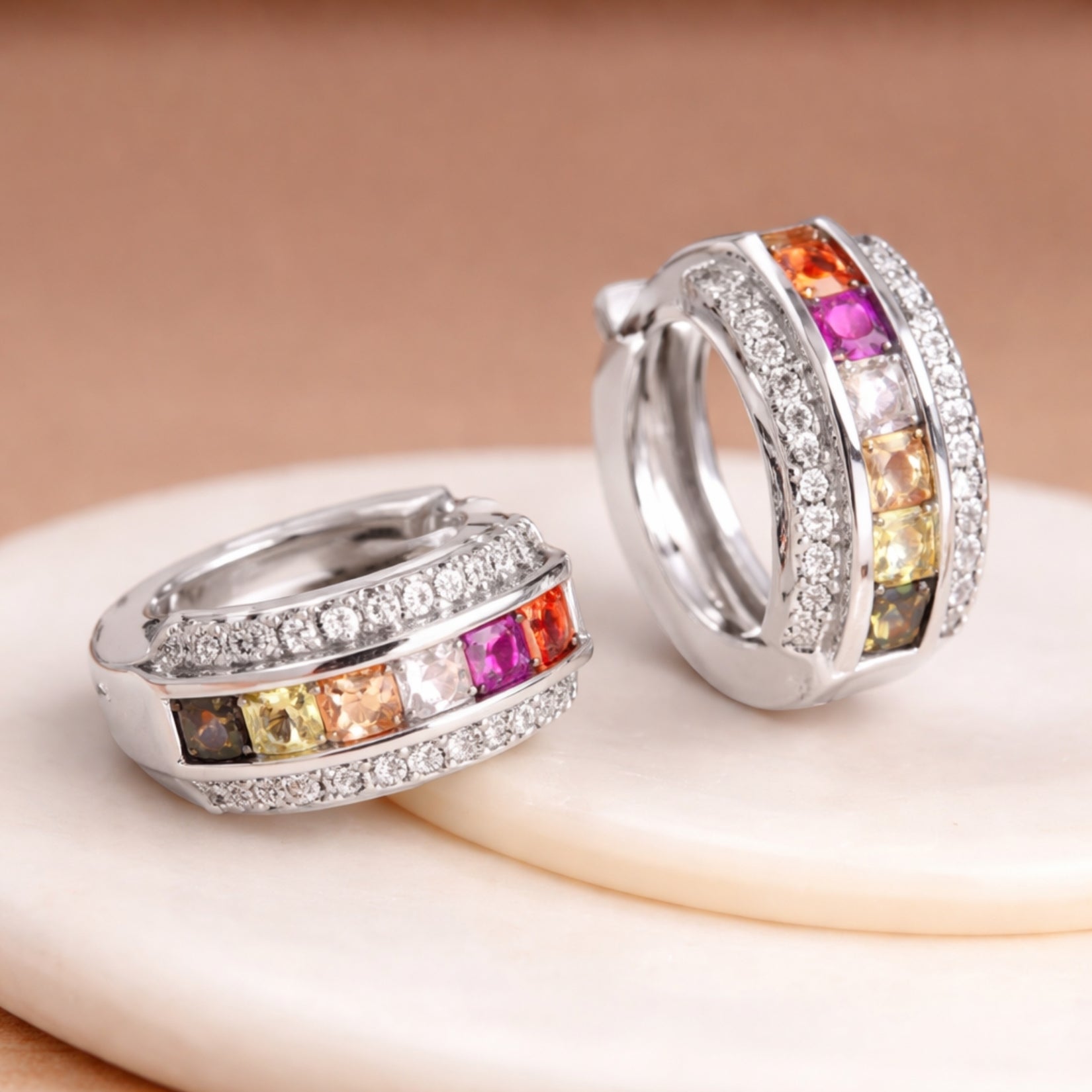 An angled view of the Kouvr Zinia rainbow sapphire earrings on a white marble surface, showcasing the craftsmanship and diamond pavé details.