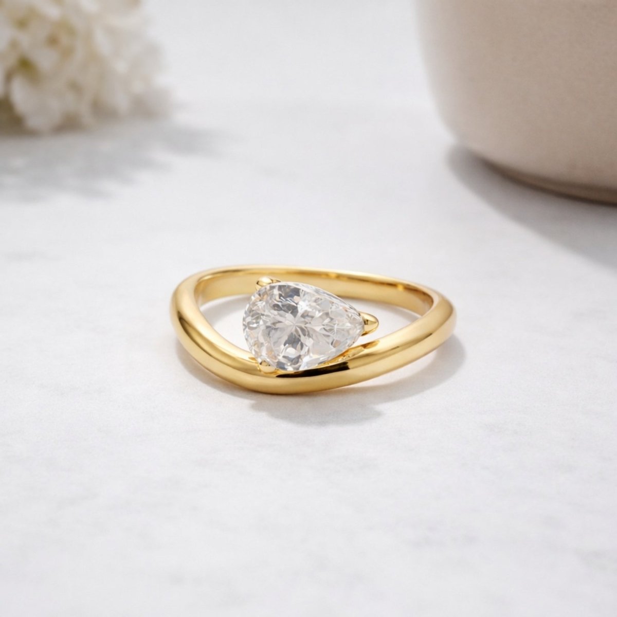 The Kouvr Zuri teardrop diamond solitaire ring in 18k yellow gold resting on a white marble surface.
