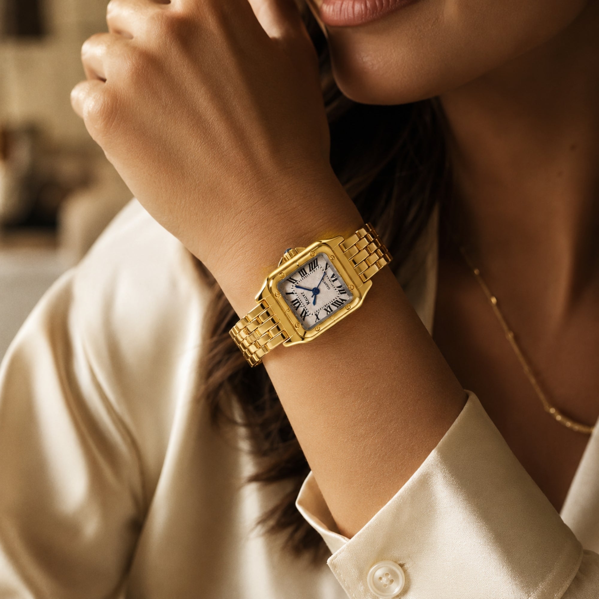 Woman's wrist wearing the Kouvr gold link dress watch with Roman numerals, paired with a delicate gold necklace and satin shirt.