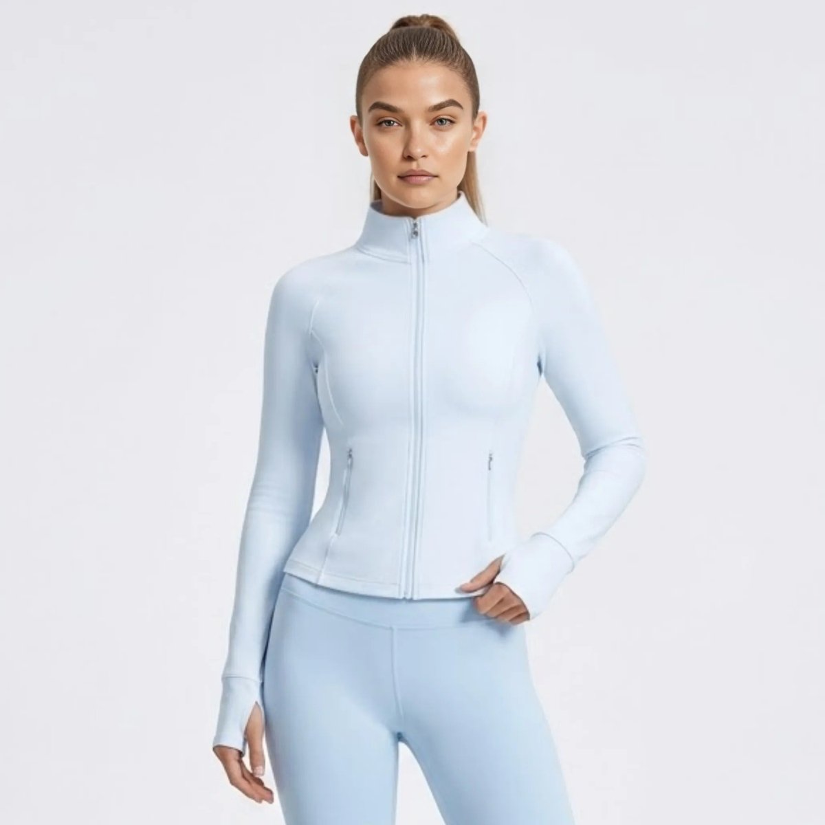 Front view of woman wearing Kouvr light blue fitted zip-up athletic jacket with mock neck.