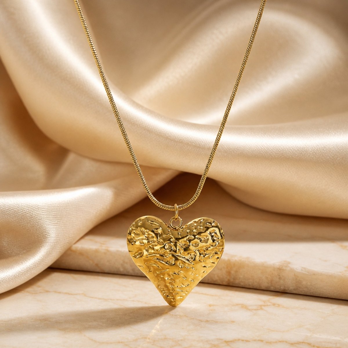 Premium gold textured heart necklace displayed elegantly against a draped champagne silk fabric background
