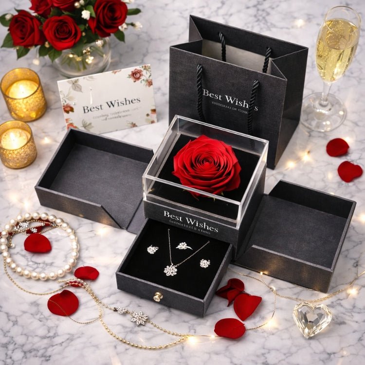 Top-down view of a complete romantic gift set including a blue gift bag, a greeting card, a preserved rose jewelry box, and a crystal heart, arranged on a marble surface with petals and candles.