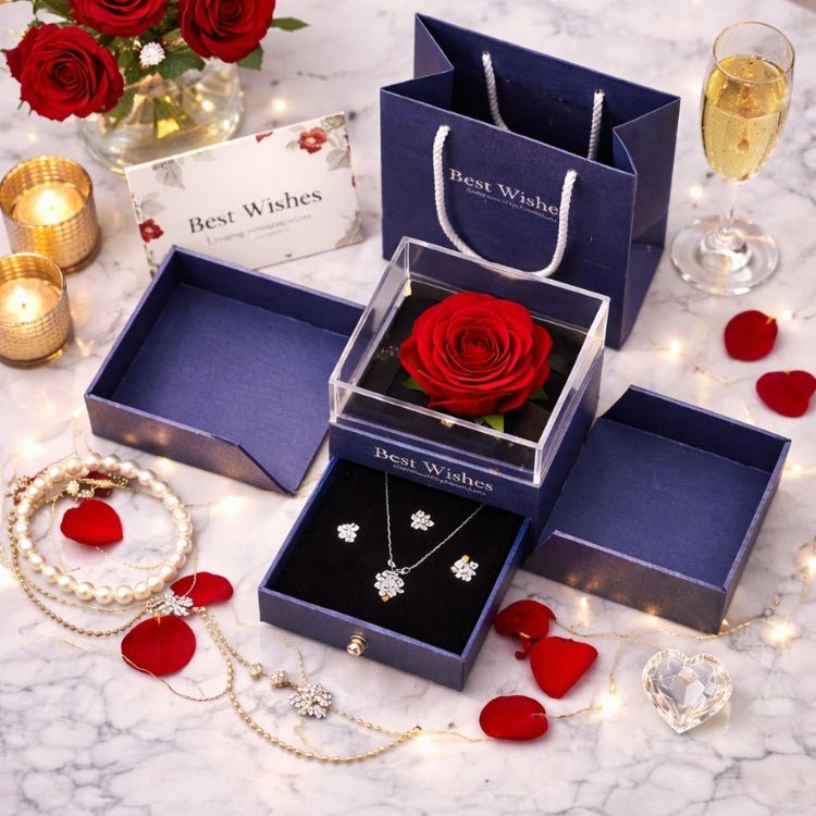 Top-down view of a complete romantic gift set including a blue gift bag, a greeting card, a preserved rose jewelry box, and a crystal heart, arranged on a marble surface with petals and candles.