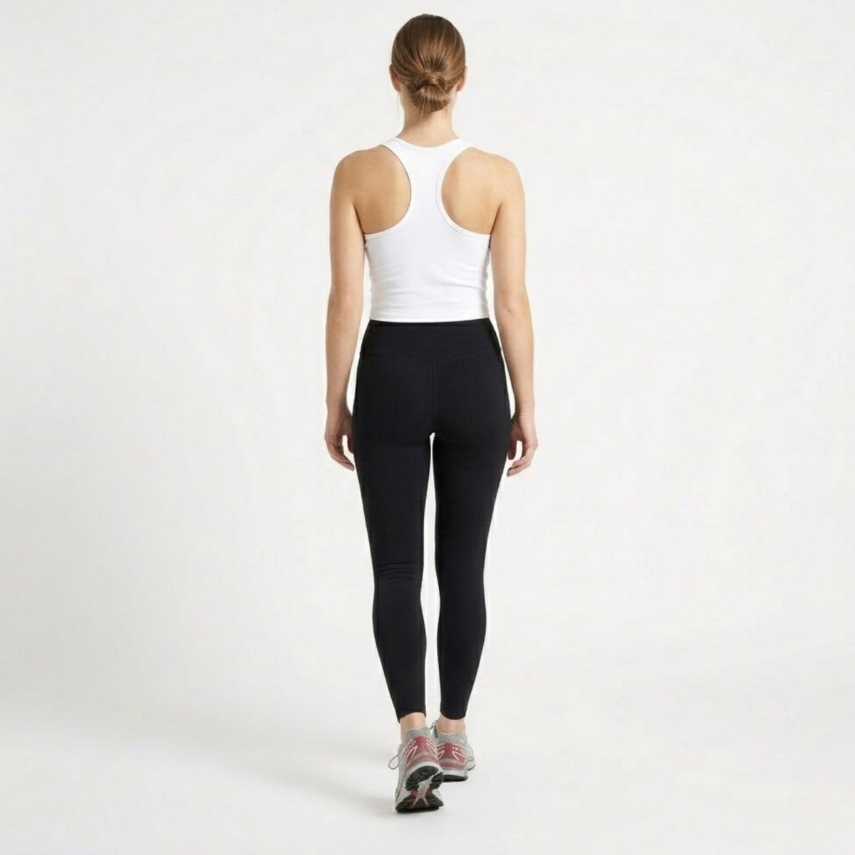 Full body back angle of woman in a white luxury fitness crop tank and black activewear bottoms.