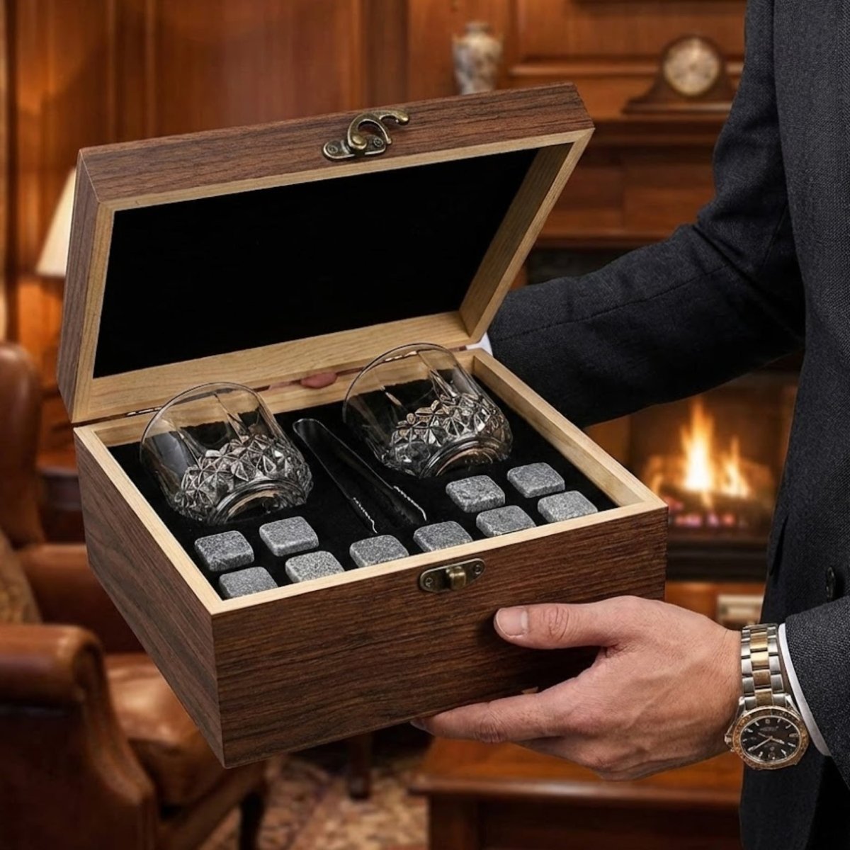 A man in a suit holding the open Kouvr whiskey stones gift box, with a warm fireplace and sophisticated living room in the background.