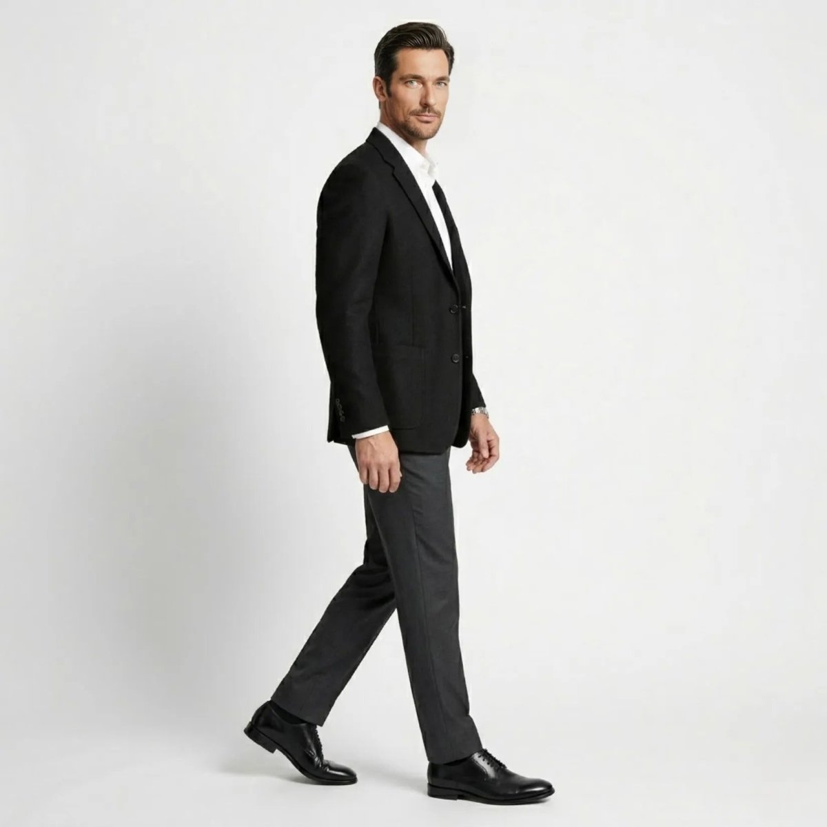Side profile of male model walking wearing a black tailored patch pocket suit jacket.