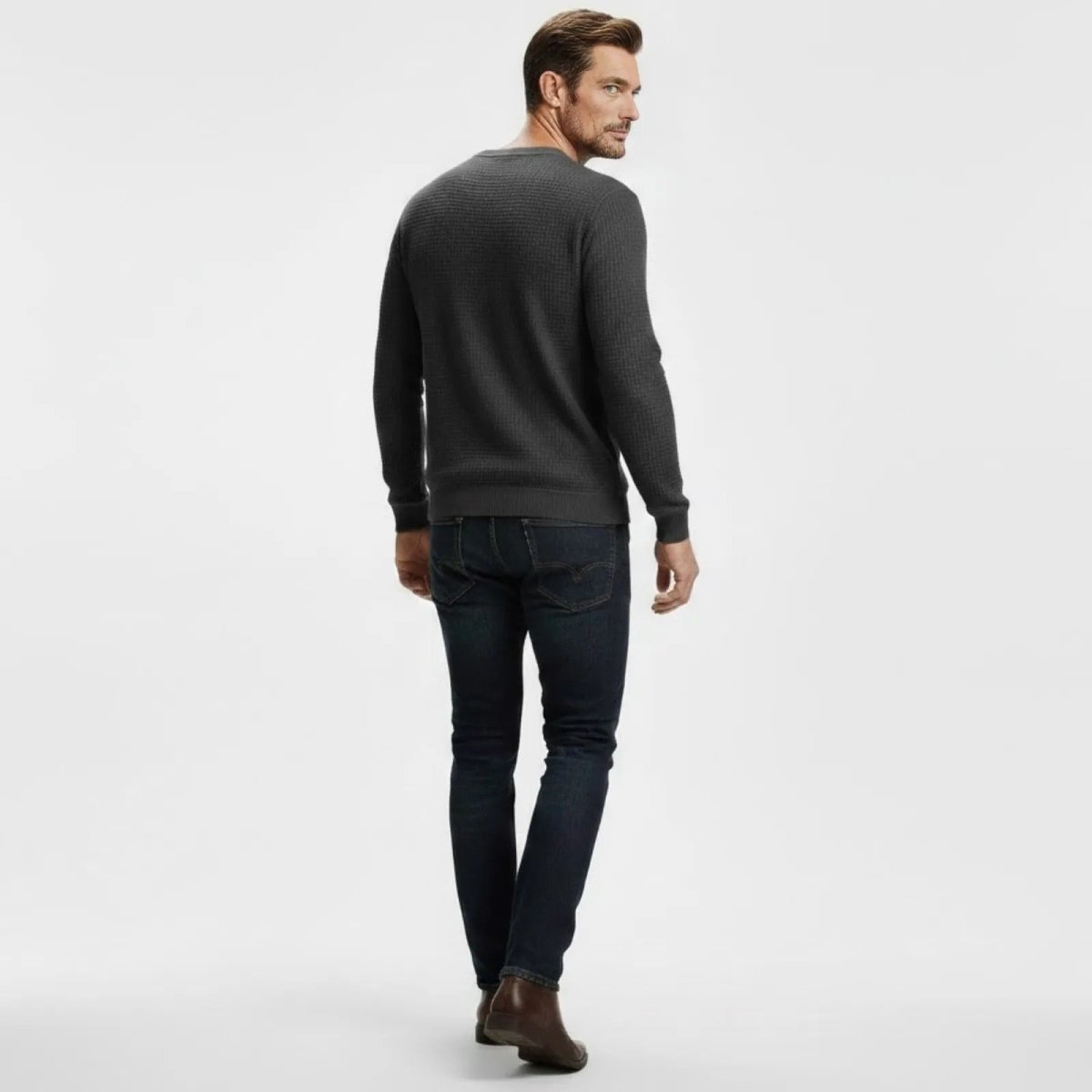 Back view of a man walking in a Kouvr Fashion dark grey waffle knit sweater and dark denim jeans.