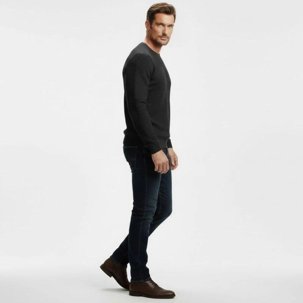 Side profile of a man in a Kouvr Fashion dark grey textured merino wool blend sweater showing its slim fit and sleeve length.