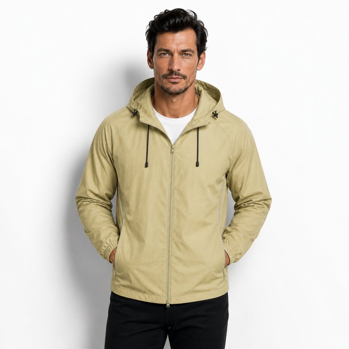 Man wearing Kouvr premium light army green lightweight hooded windbreaker jacket with hands in pockets against a white studio background.
