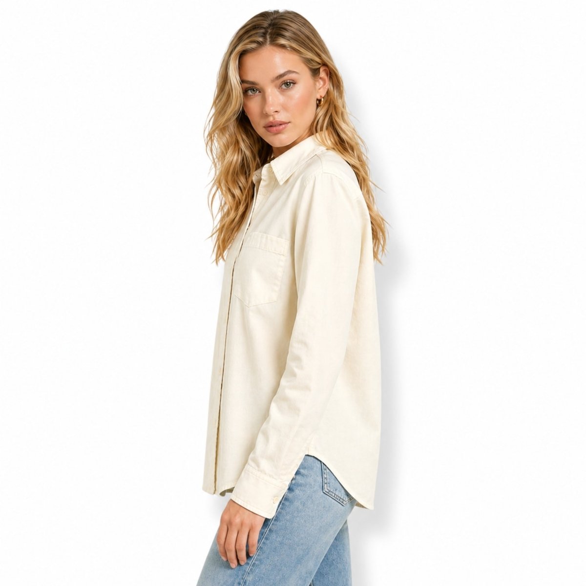 Side profile of a minimalist beige long sleeve button down blouse showing the tailored sleeve drape and relaxed fit over casual denim.