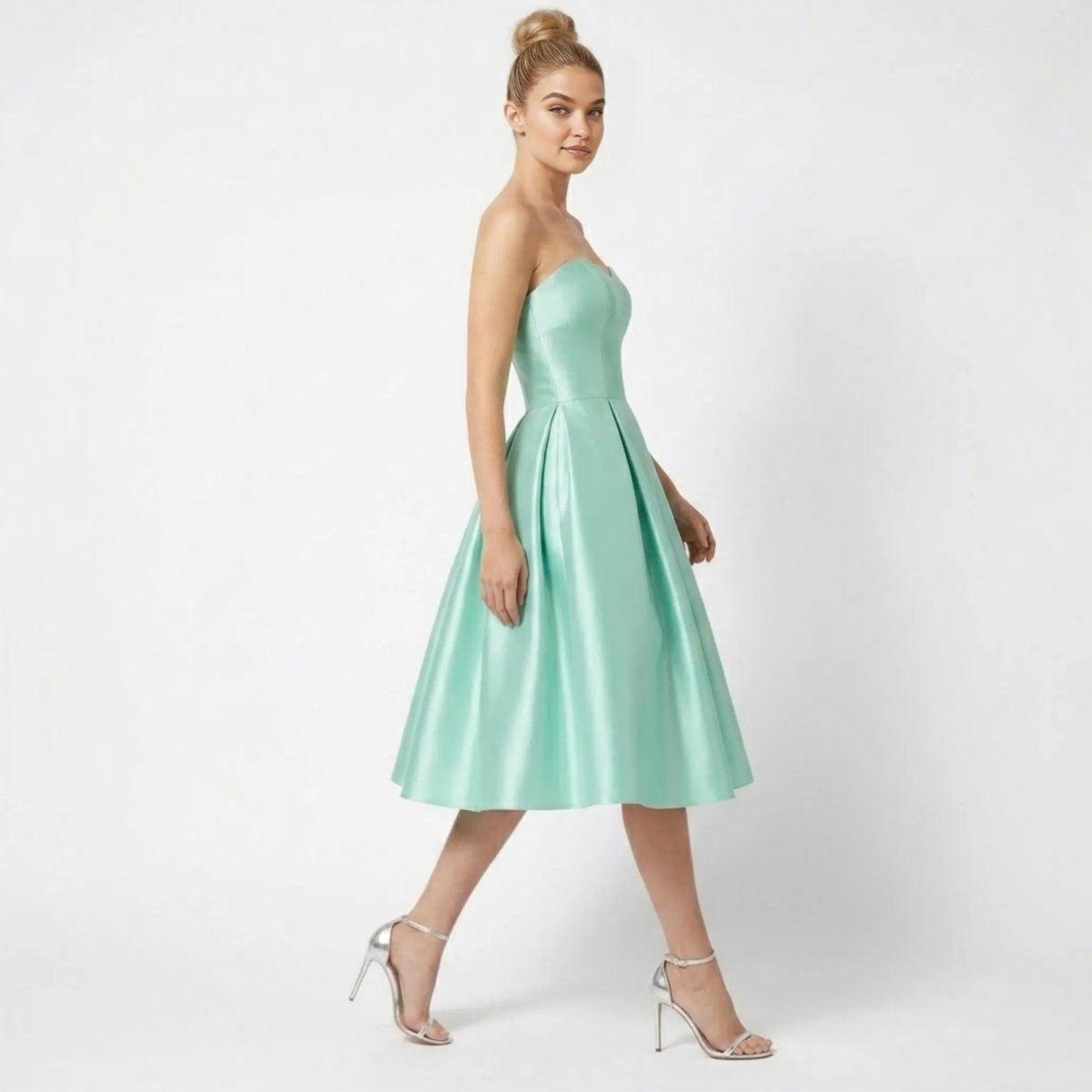 Side view of model walking in Kouvr mint green satin fit and flare pleated formal wedding guest dress
