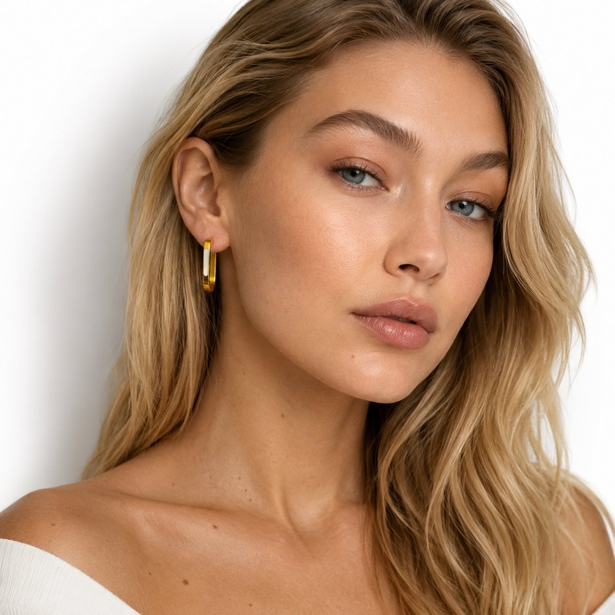 Beautiful blonde female model looking directly at the camera wearing elegant thick gold rectangular hoop earrings with natural glowing makeup.