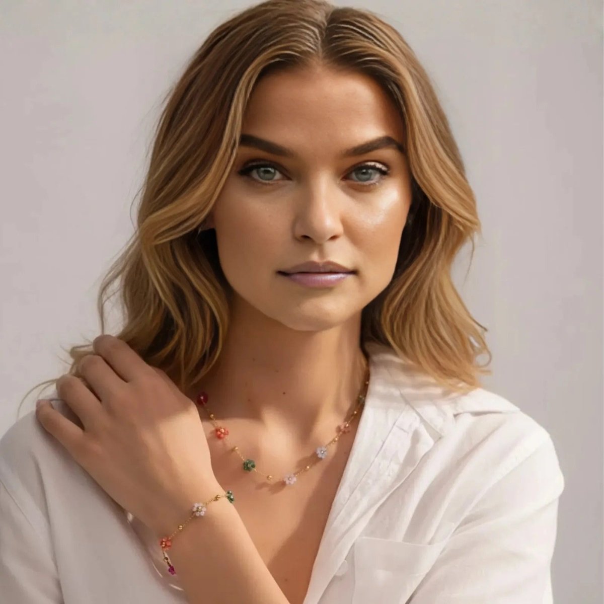 A blonde model with blue eyes gazes at the camera while wearing the Kouvr Floretta beaded flower necklace and bracelet with a classic white button-down shirt.