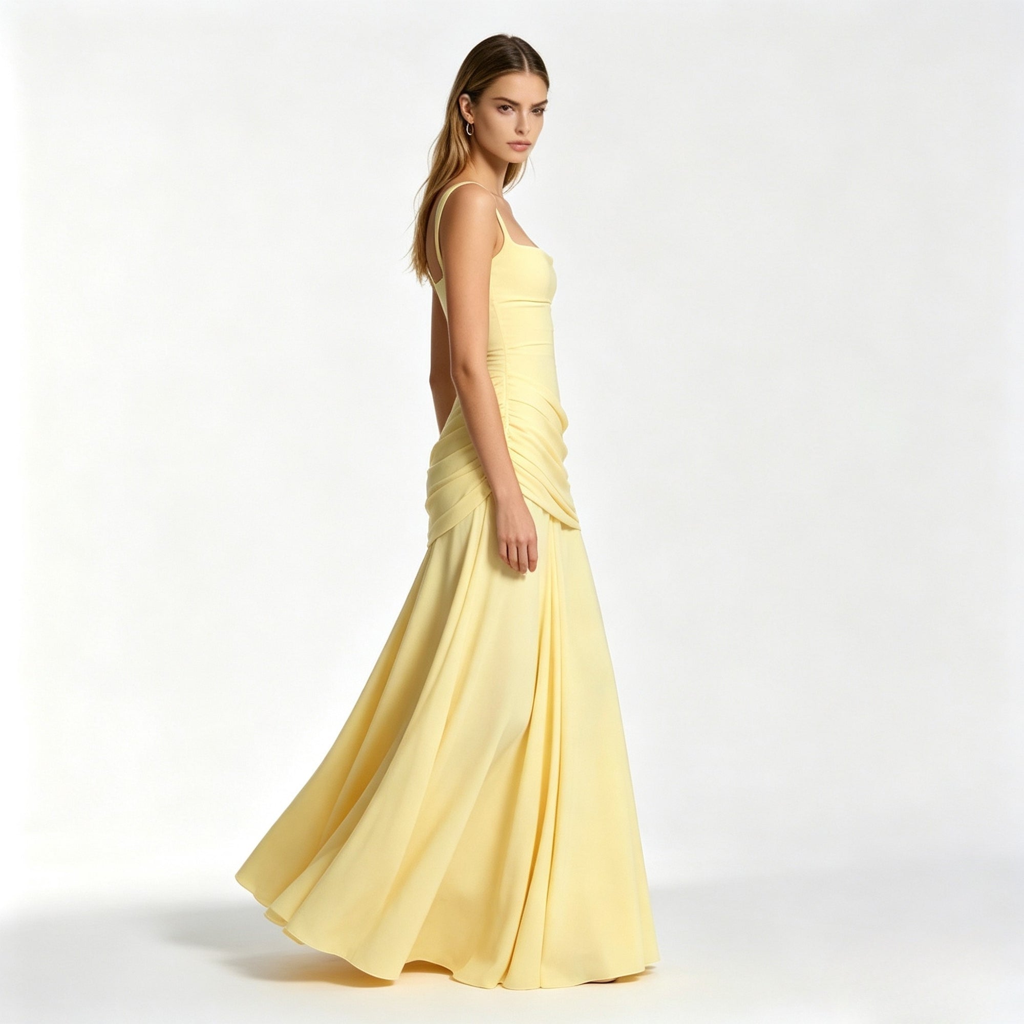 Side profile of a woman twirling in a pale yellow floor-length flowy formal maxi dress featuring asymmetrical draped hip details.