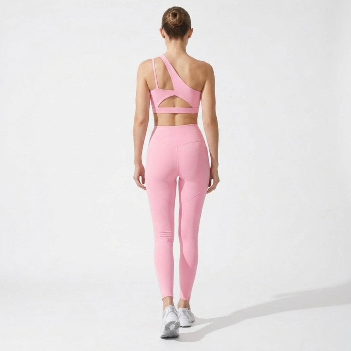 Back view showcasing the striking cutout back detail on the pink one-shoulder sports bra and contouring seams on the leggings.