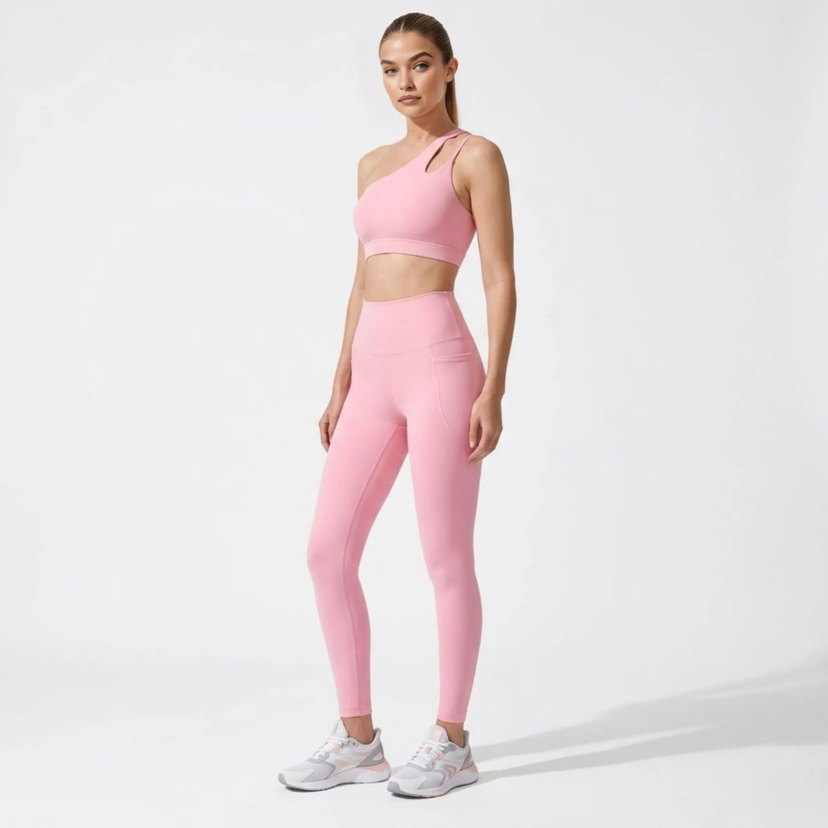 Three-quarter view highlighting the high-waisted fit and side pocket detail of the pink luxury workout leggings and asymmetrical top.