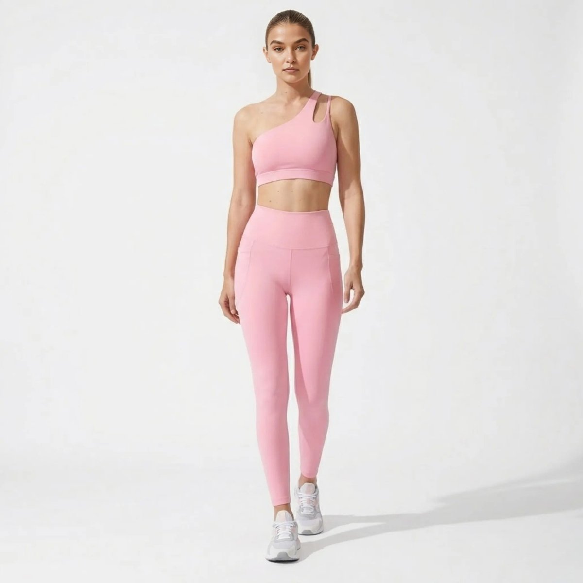 Front view of model wearing a premium pink asymmetrical one-shoulder sports bra and high-waisted leggings set with side pockets.