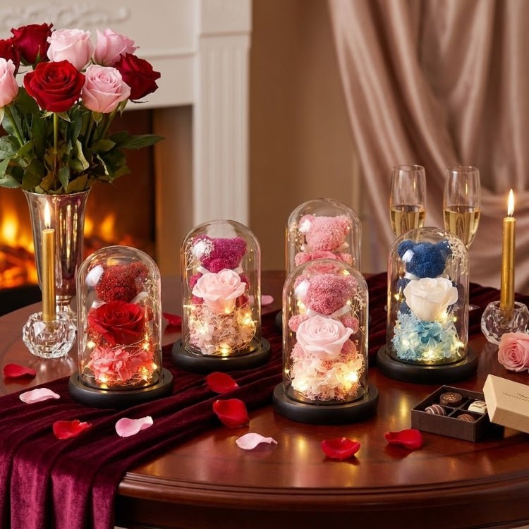 Three enchanted rose bears in purple, blue, and red sitting on decorative books with a fireplace and heart garland background.